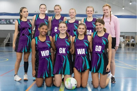 Photo of the girls netball team, all smiling on the netball court