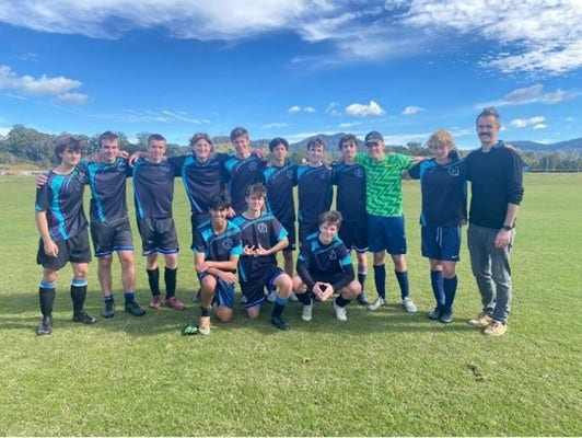 Photo of boys soccer team on the soccer pitch, in their uniform with the teacher standing on the right hand side