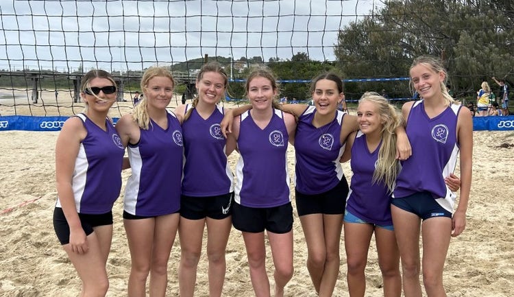 Photo of the beach volleyball girls team after a game on the beach court in their volleyball uniform